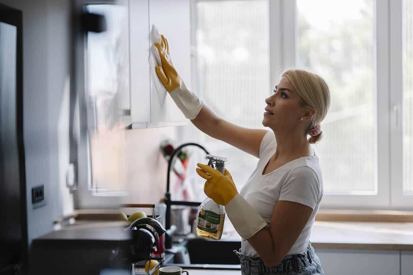 A woman cleaning kitchen cabinets in a bright kitchen