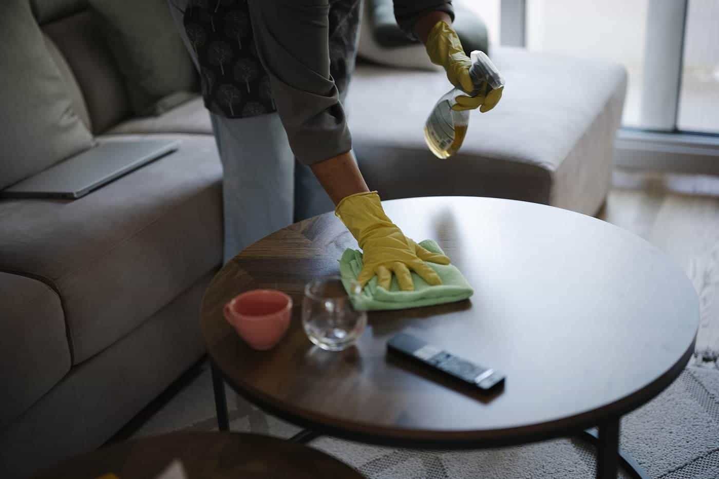 A person cleaning a coffee table with cleaning supplies