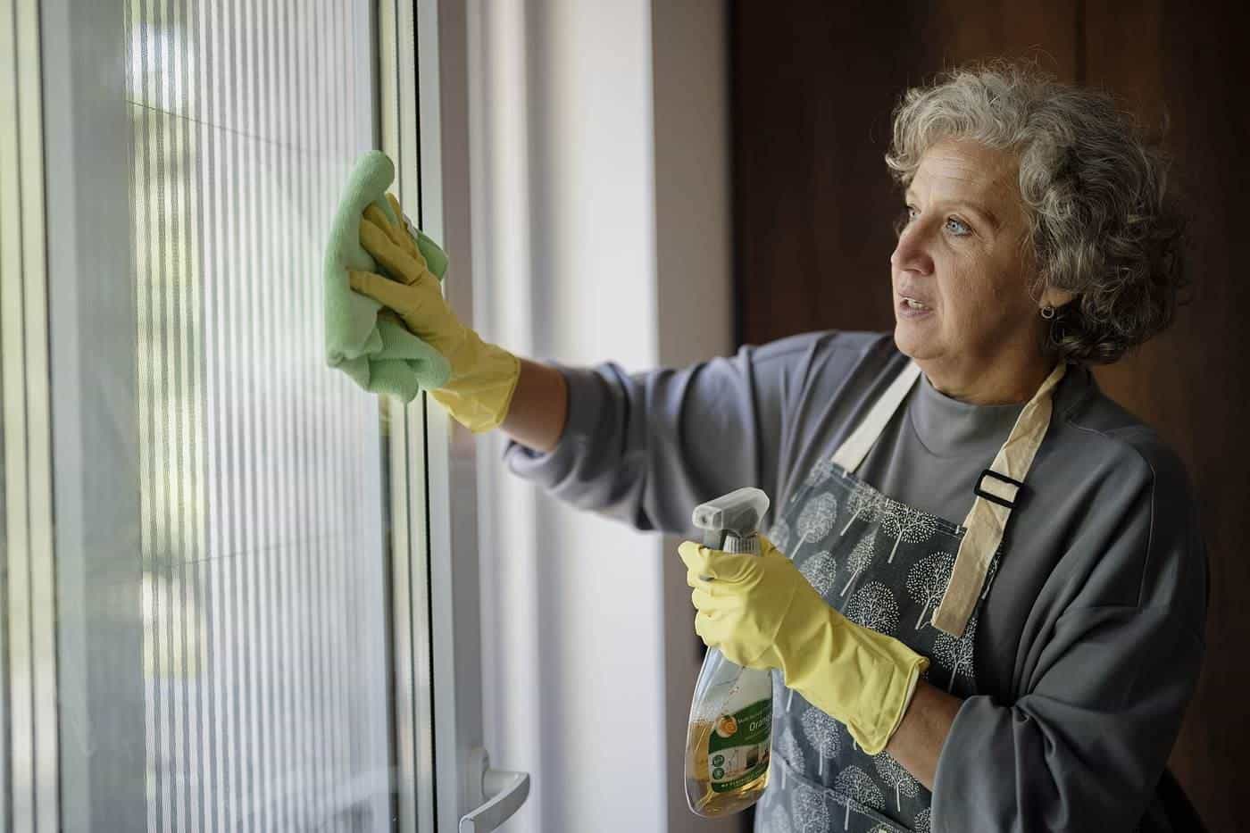 A woman cleaning a window with a cloth and spray cleaner