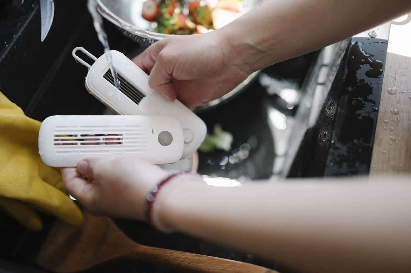 Hands holding kitchen cleaning tools at a sink