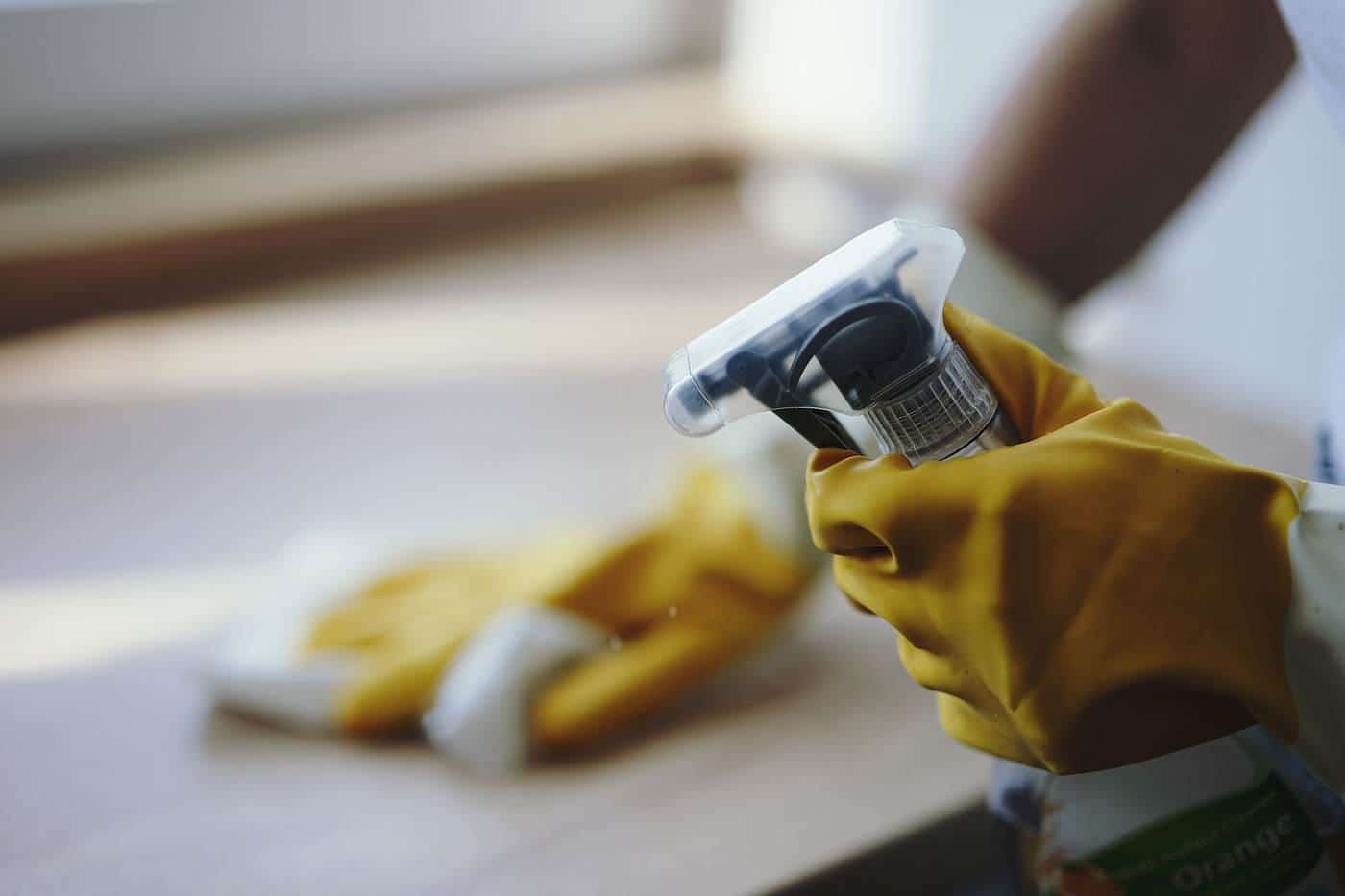 A gloved hand holding a spray bottle and cloth
