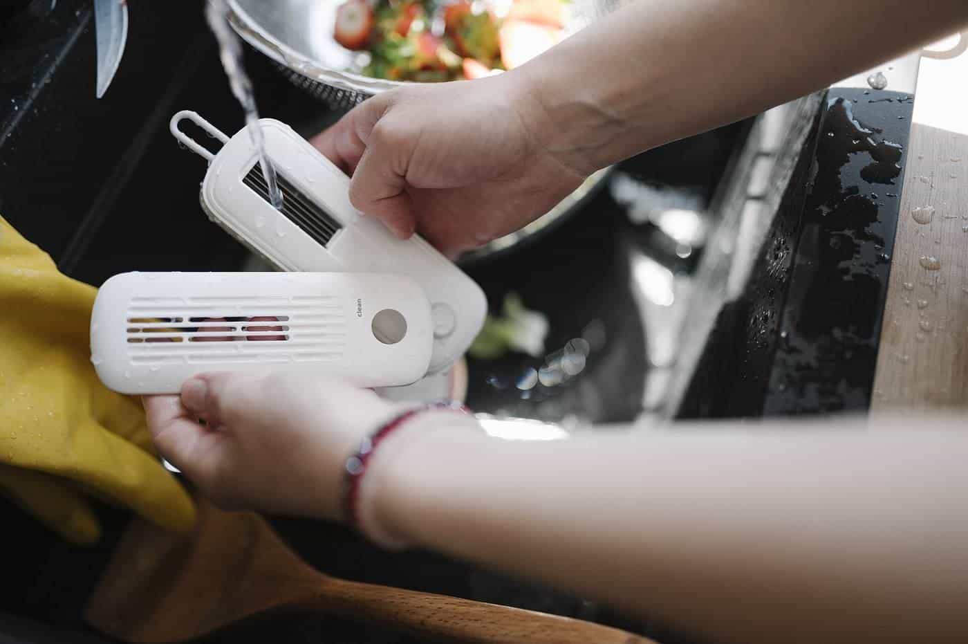 Hands holding kitchen cleaning tools at a sink