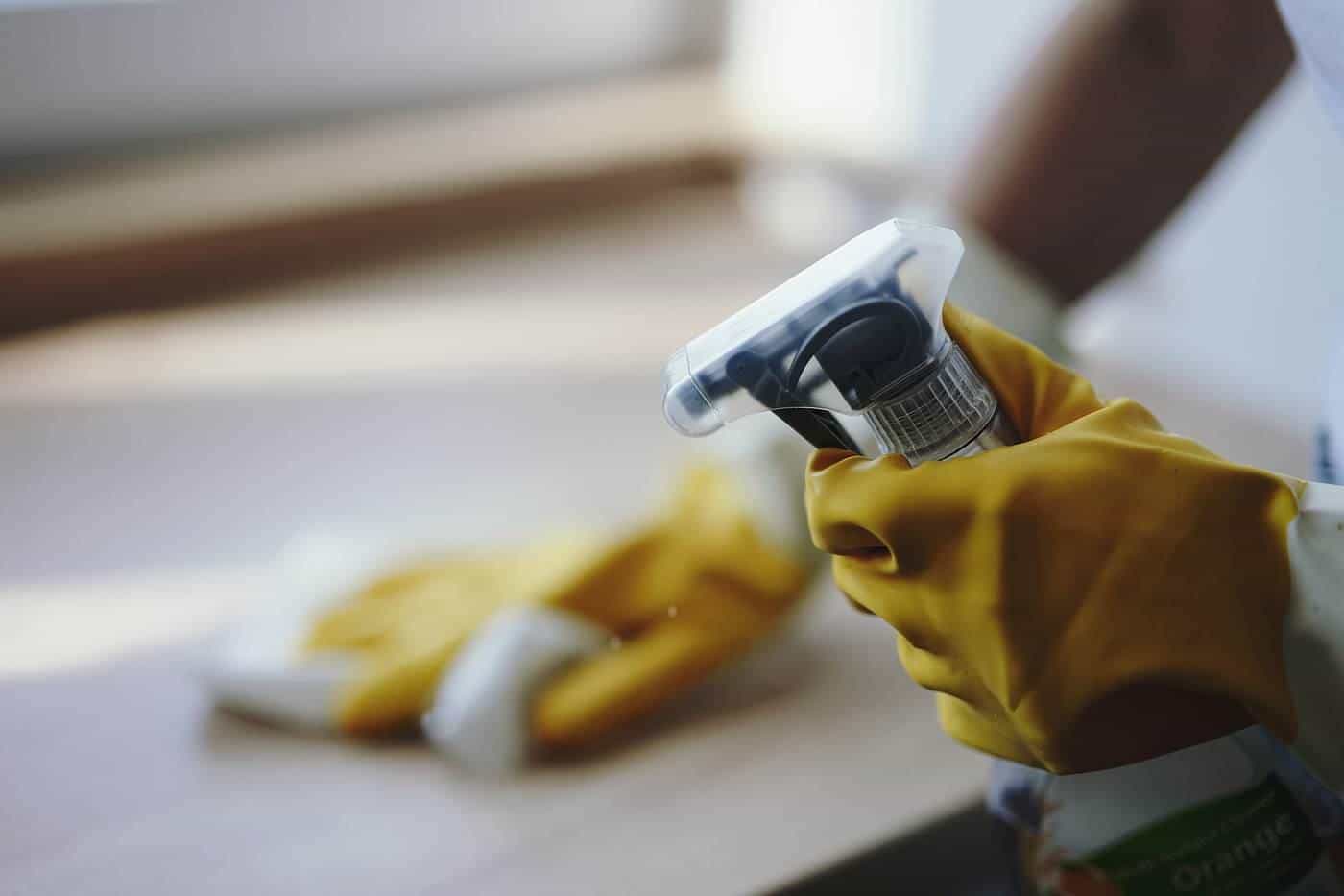 A gloved hand holding a spray bottle and cloth